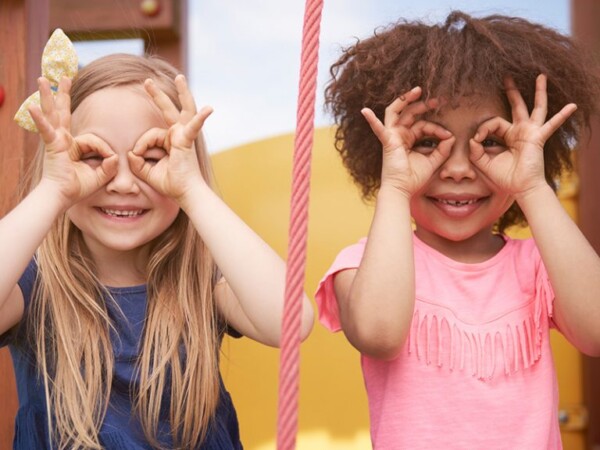 A pair of children smile while looking through their hands.